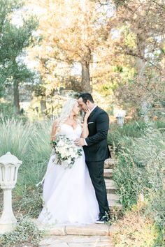 a bride and groom kissing on the steps in front of some tall grass at their wedding