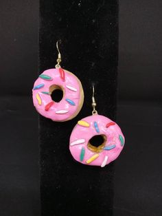 pair of pink donut earrings with sprinkles on black velvet display stand