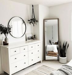 a bedroom with white furniture and plants on the dresser next to a large round mirror