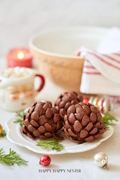 three chocolate pinecones on a plate with christmas decorations around the edges and candles in the background