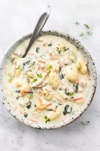 a bowl of soup with shrimp and broccoli in it on a white surface