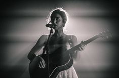 a woman holding a guitar while standing in front of a microphone and singing into a microphone