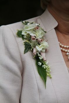 a woman wearing a white suit with flowers and pearls on her lapel flower bouquet