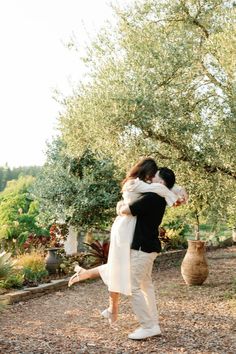 a man and woman are hugging under an olive tree in the middle of a garden