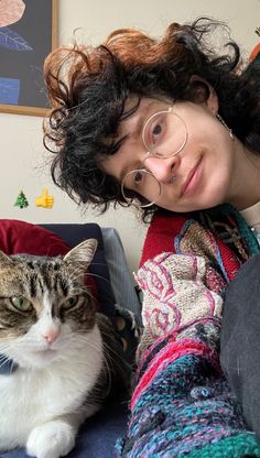 a woman sitting on a couch next to a white and gray cat with green eyes