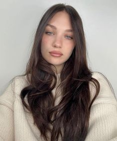 a woman with long brown hair and blue eyes is posing for the camera while wearing a white sweater