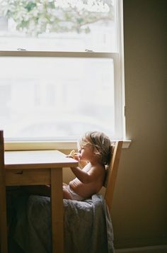 a small child sitting at a table with food in front of him and looking out the window