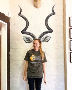 a woman standing in front of a wall with an antelope head on it