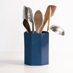 wooden spoons and utensils are in a blue cup on a white surface