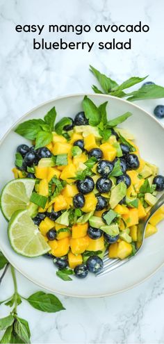 a white plate topped with blueberries, avocado and limes next to a fork