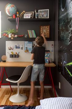 a young boy standing at a desk in front of a wall with pictures on it