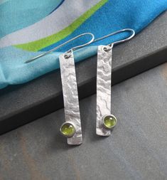 Modernist Earrings Modern, stylish and super light weight are these geometric themed earrings.  The elongated sterling silver rectangles have been imprinted with a subtle pattern and have gemstones nestled into them.   The stones are natural 6mm apple green peridot gems.  They're set in fine silver with solid silver backs. These earrings measure about 1/4" wide x 1-1/2" tall.  The total drop length from the very comfortable to wear 20 gauge sterling ear wires is about 2".   Made from 100% recycled fine and sterling silver in my Sarasota studio.   Finished to a bright sheen. Handmade by me in my Sarasota studio these arrive to you nicely gift boxed. For details on shipping, packaging and returns see shipping and policies tab above. Please visit my other shop to see more of my work: https:// Subtle Pattern, Earrings Geometric, Peridot Gemstone, Green Peridot, Apple Green, Modern Earrings, Etsy Earrings Dangle, Sarasota, Fine Silver