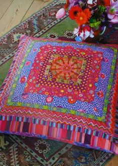 a colorful cushion sitting on top of a rug next to a vase filled with flowers