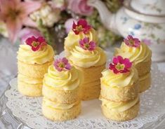 four small yellow cakes with pink flowers on top are sitting on a glass platter