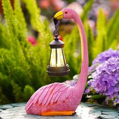 a pink flamingo standing on top of a table next to purple flowers