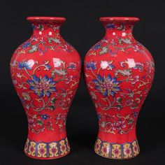 two red vases sitting side by side on top of a black surface with colorful designs