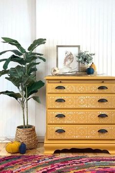 a yellow dresser sitting next to a potted plant on top of a wooden floor