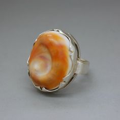 A lovely hallmarked silver ring with a polished curvy sea shell of vivid orange color. An unusual artisan handcrafted statement jewelry item from circa 1970's. The ring will be shipped in a gift box. Ring size: diameter 16.1 mm / US size: 5 1/2 / UK size: L / European - 51 3/4 Ring face measures almost 1 Inch tall (2.4 cm) - it is a true statement ring! Weight: 7.6 grams Hallmarked with a Dutch ZII hallmark for 835 continental silver Excellent vintage condition. The standard shipping for this it Unique Orange Ring Jewelry, Handmade Vintage Orange Rings, Vintage Handmade Orange Rings, Orange Hand-strung Multi-strand Jewelry, Orange Sterling Silver Ring With Polished Finish, Artisan Orange Nickel-free Jewelry, Unique Orange Cabochon Ring, Unique Hand-strung Orange Necklace, Victorian Style Jewelry