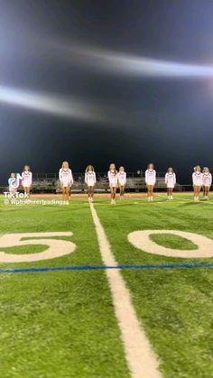 a group of women standing on top of a field next to a football field at night