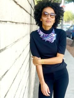 a woman leaning against a wall wearing sunglasses and a black top with purple flowers on it