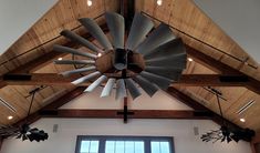 a large metal fan hanging from the ceiling in a room with wood beams and windows