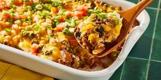 a casserole dish with meat, vegetables and cheese in it on a wooden spoon