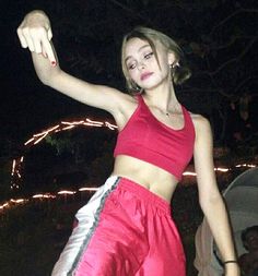 a woman in red top and silver pants holding a white frisbee at night