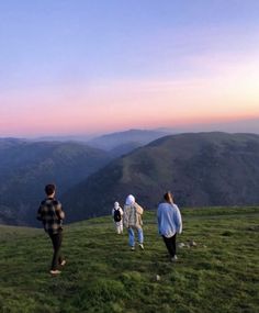 four people standing on top of a grass covered hill with mountains in the back ground