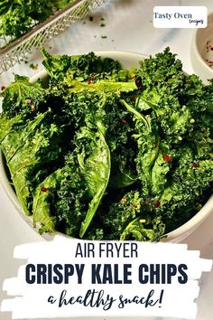 a bowl filled with green kale chips on top of a white table next to other food