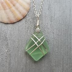 a green sea glass pendant sitting on top of a table next to a seashell