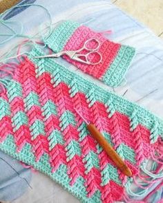 a pink and green crocheted bag sitting on top of a bed next to a pair of scissors