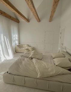 an unmade bed sitting in the middle of a room with white walls and wooden beams