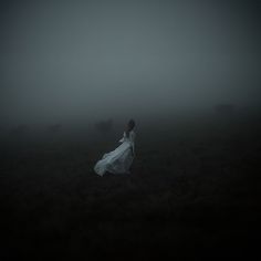 a woman in a white dress is walking through the fog