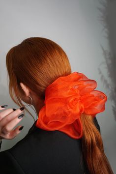 Girl with pony tail that has large red sheere double scrunhie in hair - the girl is wearing black suit and she is siting by white background Satin