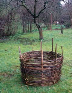 a large basket made out of branches in the middle of a grassy area next to a tree