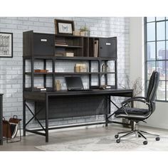 an office desk and chair in front of a white brick wall with black furniture on it