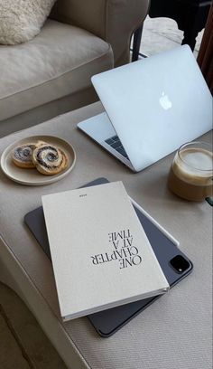 an open book sitting on top of a table next to a laptop computer and cup of coffee