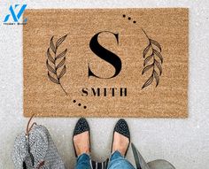 a person standing in front of a door mat with the letter s and leaves on it