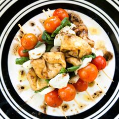 a black and white plate topped with meat and veggies on skewers