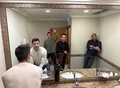 three men are standing in front of a bathroom mirror