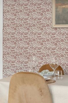 a dining room table set with place settings and wine glasses on it, in front of a floral wallpaper