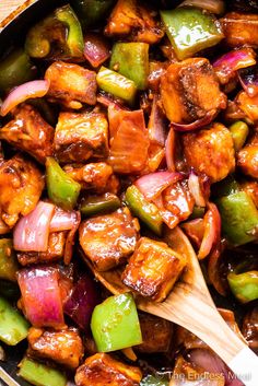 chicken and peppers stir fry in a skillet with a wooden spoon on the side