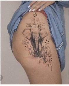 an elephant tattoo on the side of a woman's thigh, with leaves and flowers around it