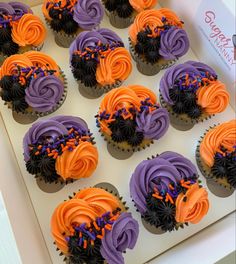 cupcakes decorated with purple and orange frosting in a white box on top of a table