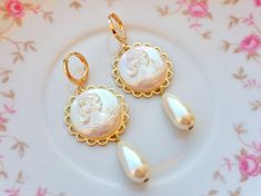 These beautiful cameo earrings were created with ornate brass settings adorned with white pearlescent Cameo cabochons and vintage teardrop pearls. These earrings hang beautifully from gold plated lever back ear wires and measure 2 1/4 inches in length and 7/8 inches in width. ~All of my listings are handmade with love and ready to ship and will arrive to you in a gift box with bow for easy gift giving~ Elegant Cameo Earrings As Gift, Gold Cameo Round Earrings, Elegant Cameo Earrings For Gift, Gold Cameo Earrings For Wedding, Elegant Cameo Earrings For Wedding, Elegant Round Cameo Earrings, Elegant Cameo Clip-on Earrings Gift, Gold Cameo Drop Earrings, Cameo Drop Earrings For Wedding