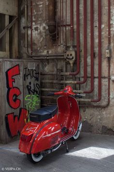 a red scooter is parked in front of some pipes