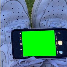 a cell phone with a green screen in someone's white tennis shoes on the grass