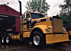 a yellow semi truck parked in front of a red building with a cat sign on it's side