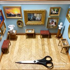 a pair of scissors sitting on top of a hard wood floor in front of paintings