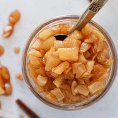 a glass jar filled with apple slices on top of a white countertop next to spoons